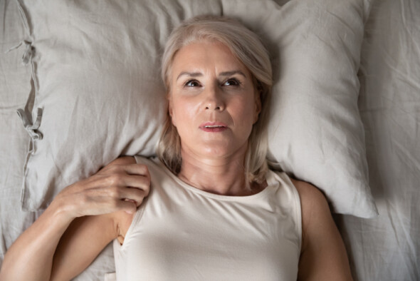 Mature woman lying on bed deep in thought