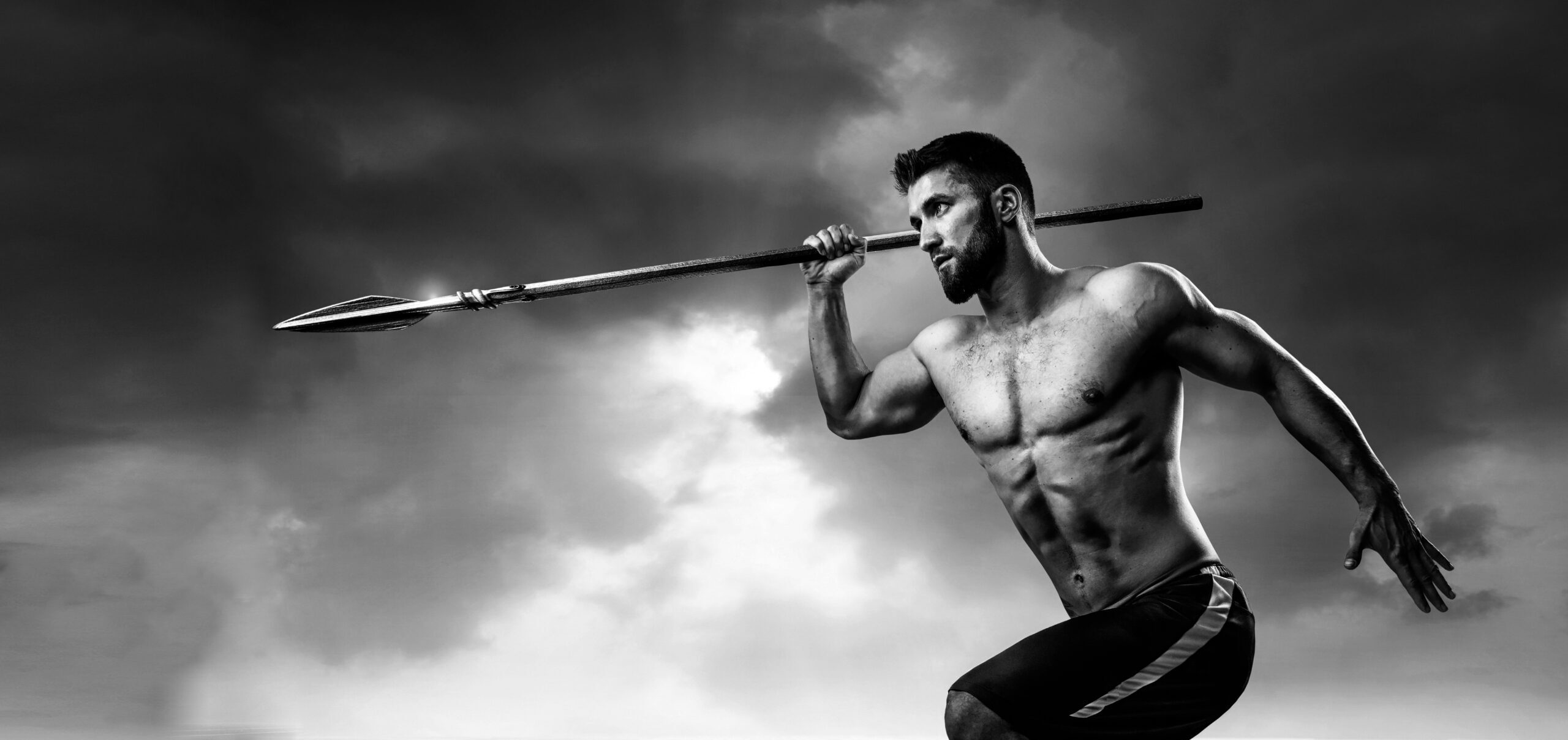 Topless man in shorts running with spear