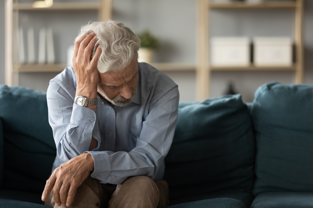 Mature man looking stressed and anxious sat on blue sofa