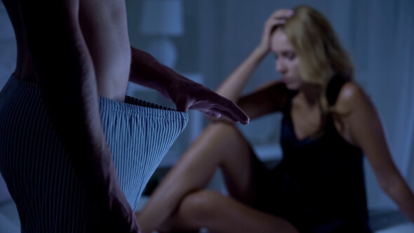 Man looking down trousers with stressed woman in background