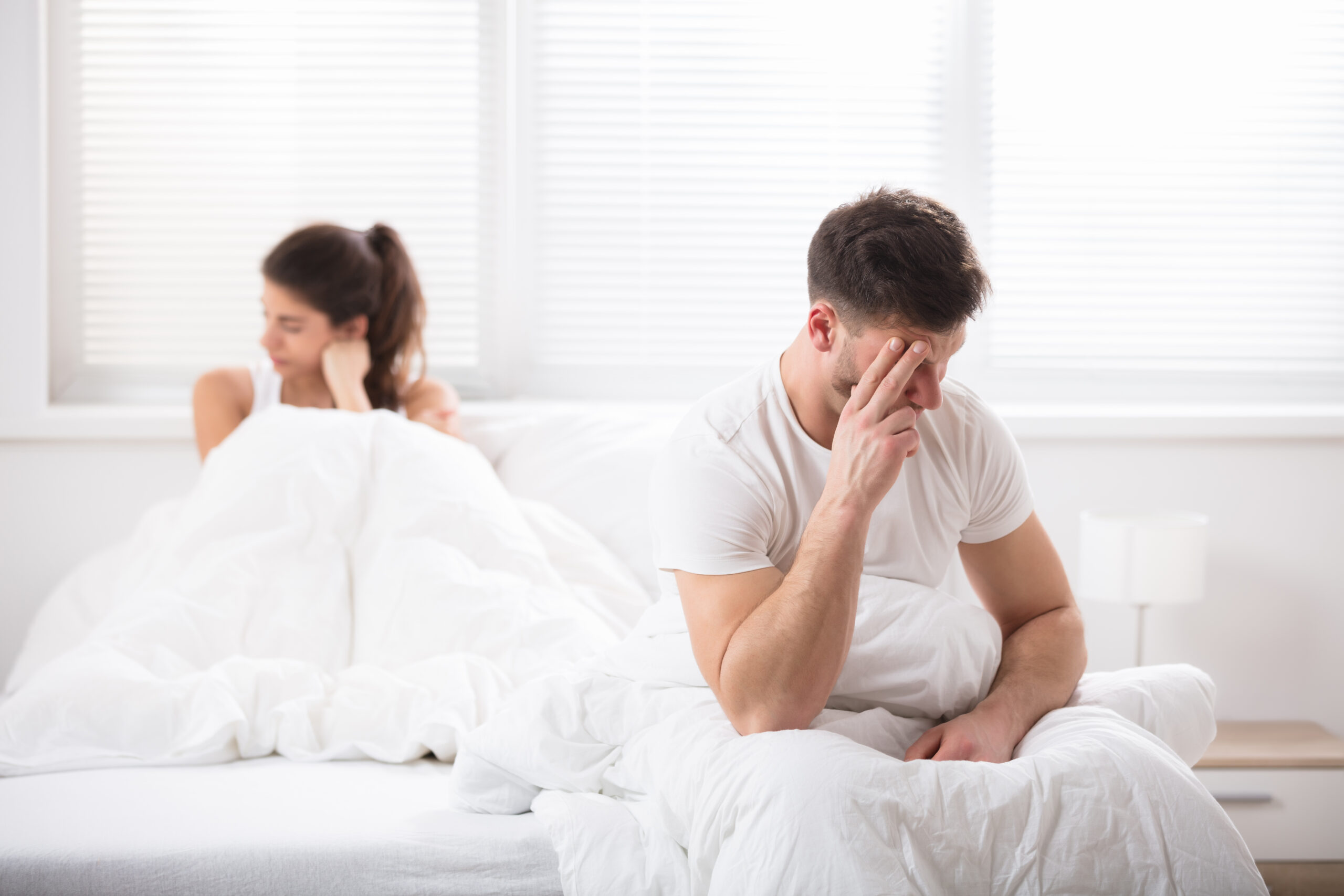 Embarrassed couple sitting apart on white bed