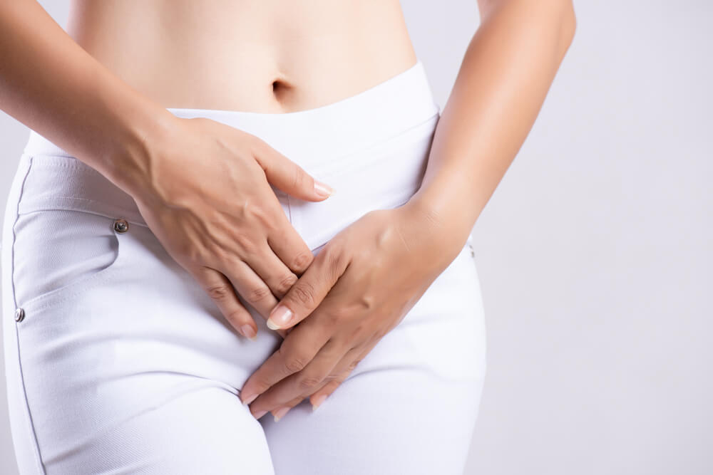 Young woman experiencing abdominal discomfort, highlighting common symptoms like vaginal dryness or postmenopausal issues addressed by laser vaginal rejuvenation treatments